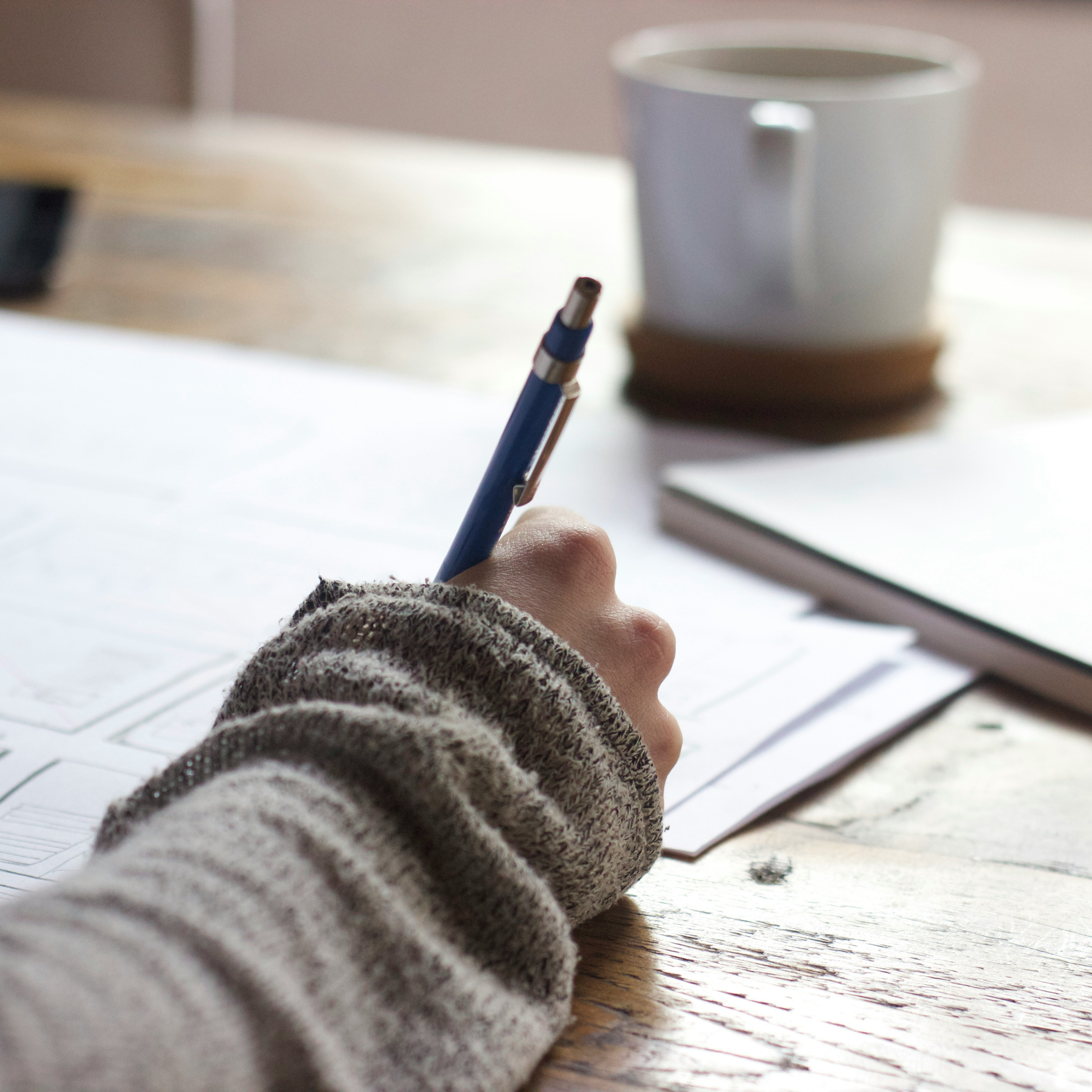Close up shot of woman writing on a pad of paper with a coffee in the background